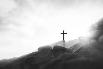 An open Bible with a cross on top, depicted in black and white.